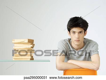 Stock Image - Young man sitting next to stack of books, portrait. Fotosearch