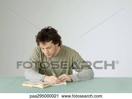 Young man sitting with open book, taking notes View Large Photo Image Stock Image - Young man sitting with open book, taking notes. Fotosearch