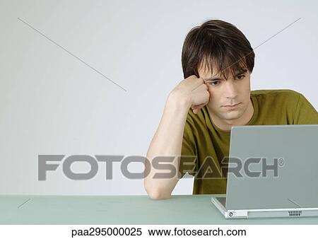Young man using laptop, leaning on elbow View Large Photo Image Stock Photography - Young man using laptop, leaning on elbow. Fotosearch