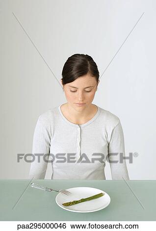Young woman looking down at plate with single asparagus View Large Photo Image Stock Photograph - Young woman looking down at plate with single asparagus. Fotosearch