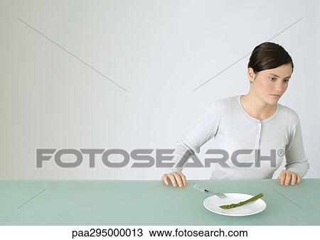 Young woman sitting at table, in front of plate with single asparagus View Large Photo Image Stock Image - Young woman sitting at table, in front of plate with single asparagus. Fotosearch