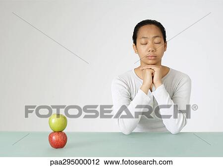 Young woman sitting with eyes shut, two apples stacked in front of her View Large Photo Image Stock Image - Young woman sitting with eyes shut, two apples stacked in front of her. Fotosearch