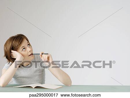 Young woman sitting with open notebook, holding pencil to mouth View Large Photo Image Stock Photo - Young woman sitting with open notebook, holding pencil to mouth. Fotosearch