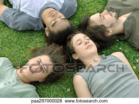Stock Photo - Four friends lying on grass with heads together. Fotosearch