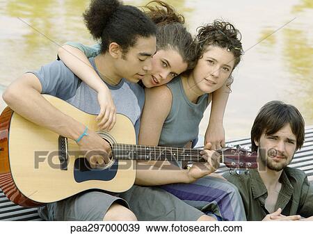 Four young friends gathered around guitar View Large Photo Image Stock Photo - Four young friends gathered around guitar. Fotosearch