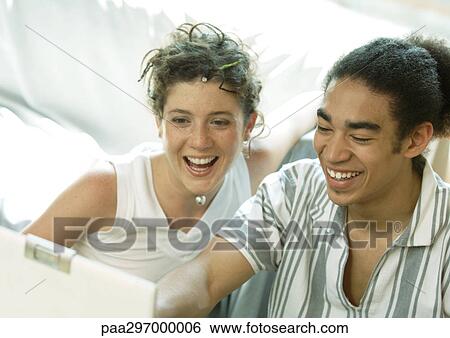Stock Photograph - Young couple looking at laptop, smiling. Fotosearch