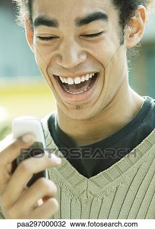 Young man laughing and looking at cell phone, close-up View Large Photo Image Stock Image - Young man laughing and looking at cell phone, close-up. Fotosearch