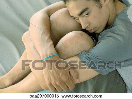 Young man sitting with arms around knees View Large Photo Image Stock Photography - Young man sitting with arms around knees. Fotosearch