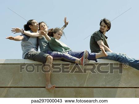 Young people sitting on top of wall with arms out View Large Photo Image Stock Image - Young people sitting on top of wall with arms out. Fotosearch