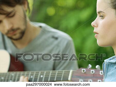 Young woman listening to young man playing guitar View Large Photo Image Picture - Young woman listening to young man playing guitar. Fotosearch