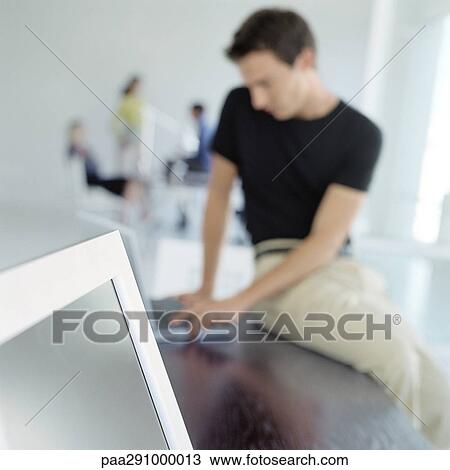 Man sitting on edge of desk in office View Large Photo Image Stock Image - Man sitting on edge of desk in office. Fotosearch