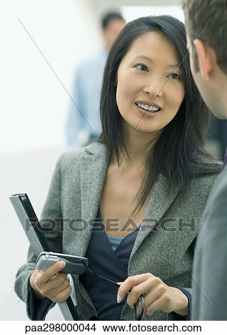 Businesswoman holding cell phone, speaking to man View Large Photo Image Picture - Businesswoman holding cell phone, speaking to man. Fotosearch