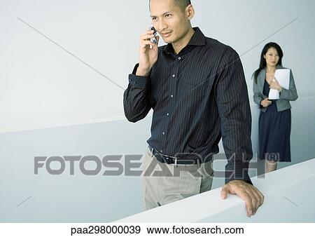 Man using cell phone, woman standing behind him View Large Photo Image Stock Photo - Man using cell phone, woman standing behind him. Fotosearch