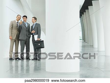 Three businessmen looking at cell phone in lobby View Large Photo Image Stock Photo - Three businessmen looking at cell phone in lobby. Fotosearch