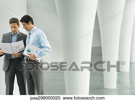 Two businessmen looking at documents in lobby View Large Photo Image Stock Image - Two businessmen looking at documents in lobby. Fotosearch