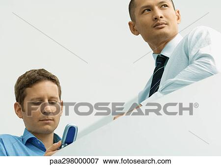 Two businessmen, one looking at cell phone View Large Photo Image Stock Photo - Two businessmen, one looking at cell phone. Fotosearch