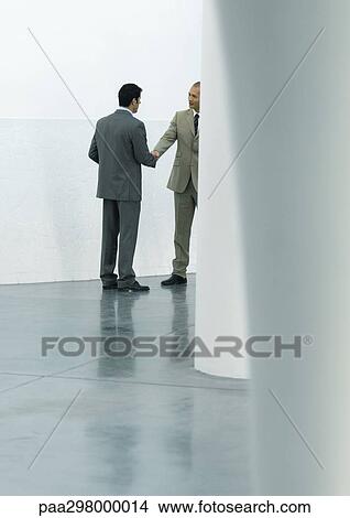 Picture - Two businessmen shaking hands in lobby. Fotosearch