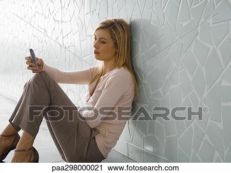 Woman sitting on floor, leaning against wall and looking at cell phone View Large Photo Image Stock Image - Woman sitting on floor, leaning against wall and looking at cell phone. Fotosearch