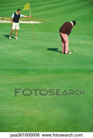 Golfer putting while second man holds golf flag View Large Photo Image Stock Photo - Golfer putting while second man holds golf flag. Fotosearch