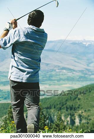 Stock Image - Golfer swinging, overlooking landscape. Fotosearch