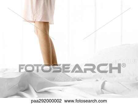 Stock Image - Woman standing on bed, low section. Fotosearch