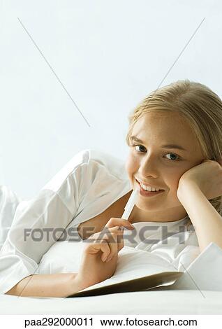Stock Image - Young woman lying down with pen to lips. Fotosearch