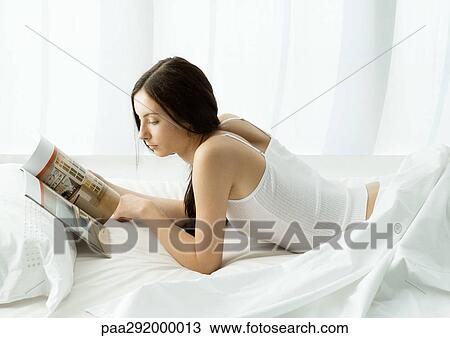 Young woman lying in bed looking at magazine View Large Photo Image Stock Image - Young woman lying in bed looking at magazine. Fotosearch