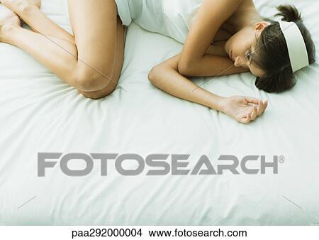 Picture - Young woman lying on bed with eyes open. Fotosearch
