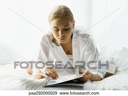 Young woman sitting in bed, leaning forward and reading View Large Photo Image Stock Photo - Young woman sitting in bed, leaning forward and reading. Fotosearch