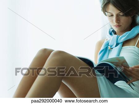 Young woman sitting with knees up, reading magazine View Large Photo Image Stock Image - Young woman sitting with knees up, reading magazine. Fotosearch