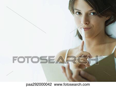 Young woman with pen to lips, holding notebook View Large Photo Image Stock Image - Young woman with pen to lips, holding notebook. Fotosearch