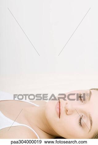 Stock Photo - Woman lying down with eyes closed, close-up. Fotosearch
