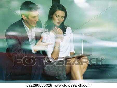 Businessman and businesswoman sitting together, looking at laptop View Large Photo Image Stock Photo - Businessman and businesswoman sitting together, looking at laptop. Fotosearch