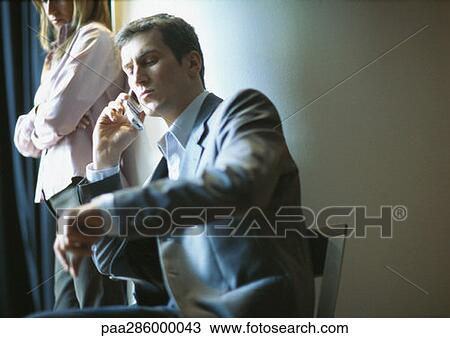 Businessman on phone, checking time, woman standing next to him View Large Photo Image Stock Image - Businessman on phone, checking time, woman standing next to him. Fotosearch