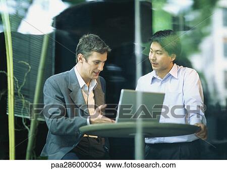 Businessmen sitting at cafe table, talking over laptop View Large Photo Image Picture - Businessmen sitting at cafe table, talking over laptop. Fotosearch