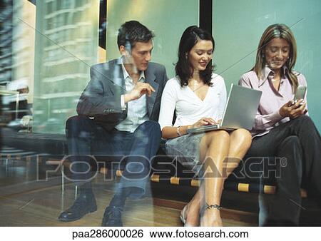 Businesspeople sitting on bench, using laptop and cellphone View Large Photo Image Stock Photograph - Businesspeople sitting on bench, using laptop and cellphone. Fotosearch