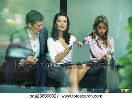 Businesswoman sitting between co-workers, looking up from laptop View Large Photo Image Stock Photo - Businesswoman sitting between co-workers, looking up from laptop. Fotosearch