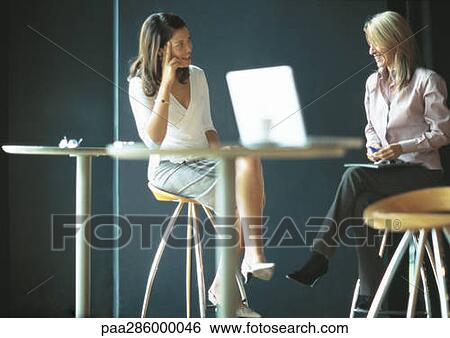 Businesswomen sitting and talking in cafe setting View Large Photo Image Stock Photograph - Businesswomen sitting and talking in cafe setting. Fotosearch
