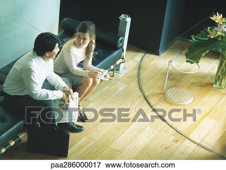 Stock Photo - Man and woman sitting on bench in lobby, high angle view. Fotosearch