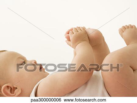 Stock Photograph - Baby lying down, holding foot. Fotosearch