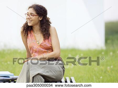 Female student sitting on bench, smiling View Large Photo Image Picture - Female student sitting on bench, smiling. Fotosearch