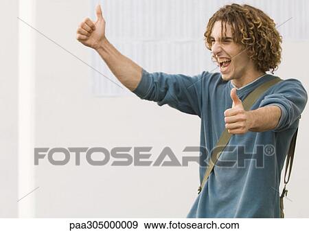 Stock Photo - Student making thumbs up sign and shouting with joy, in front of results on wall. Fotosearch