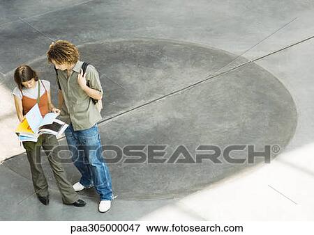 Two students standing in lobby looking at notebook together View Large Photo Image Stock Photo - Two students standing in lobby looking at notebook together. Fotosearch