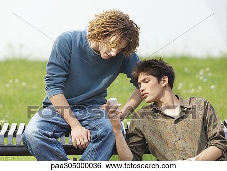 Two young men looking at cell phone View Large Photo Image Stock Photograph - Two young men looking at cell phone. Fotosearch