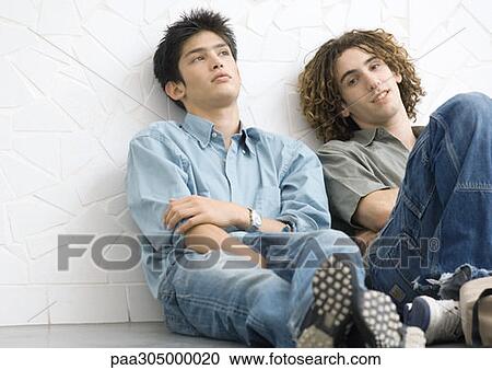 Two young men sitting on ground, leaning back against wall View Large Photo Image Stock Image - Two young men sitting on ground, leaning back against wall. Fotosearch