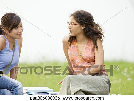 Two young women sitting on bench together, talking View Large Photo Image Stock Photography - Two young women sitting on bench together, talking. Fotosearch