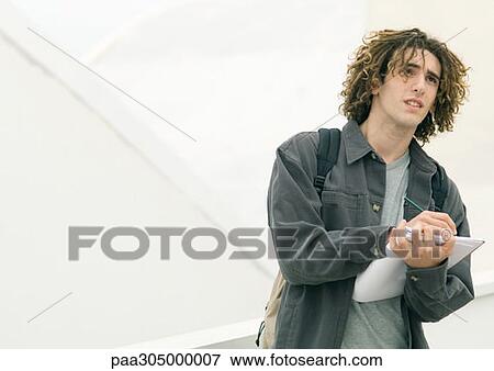 Young man standing with notebook, taking notes View Large Photo Image Stock Photo - Young man standing with notebook, taking notes. Fotosearch
