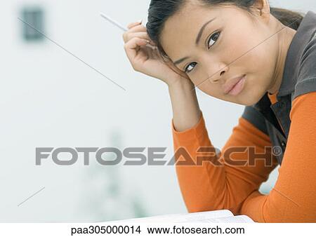 Young woman leaning on elbow, holding pen in hand View Large Photo Image Picture - Young woman leaning on elbow, holding pen in hand. Fotosearch