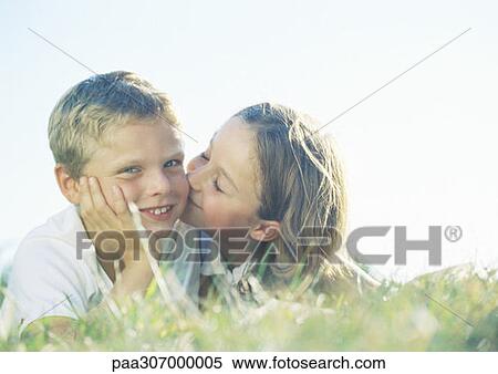 Stock Photography - Boy and girl lying on grass, girl kissing boy on cheek. Fotosearch