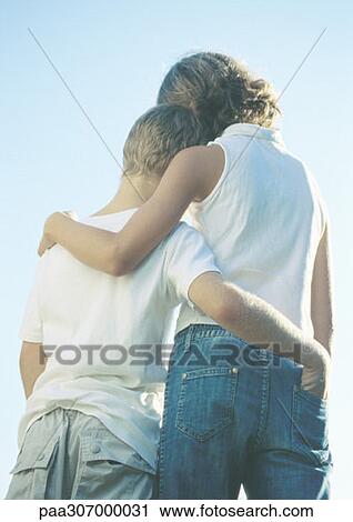 Stock Image - Boy and girl standing side by side with arms around each other. Fotosearch